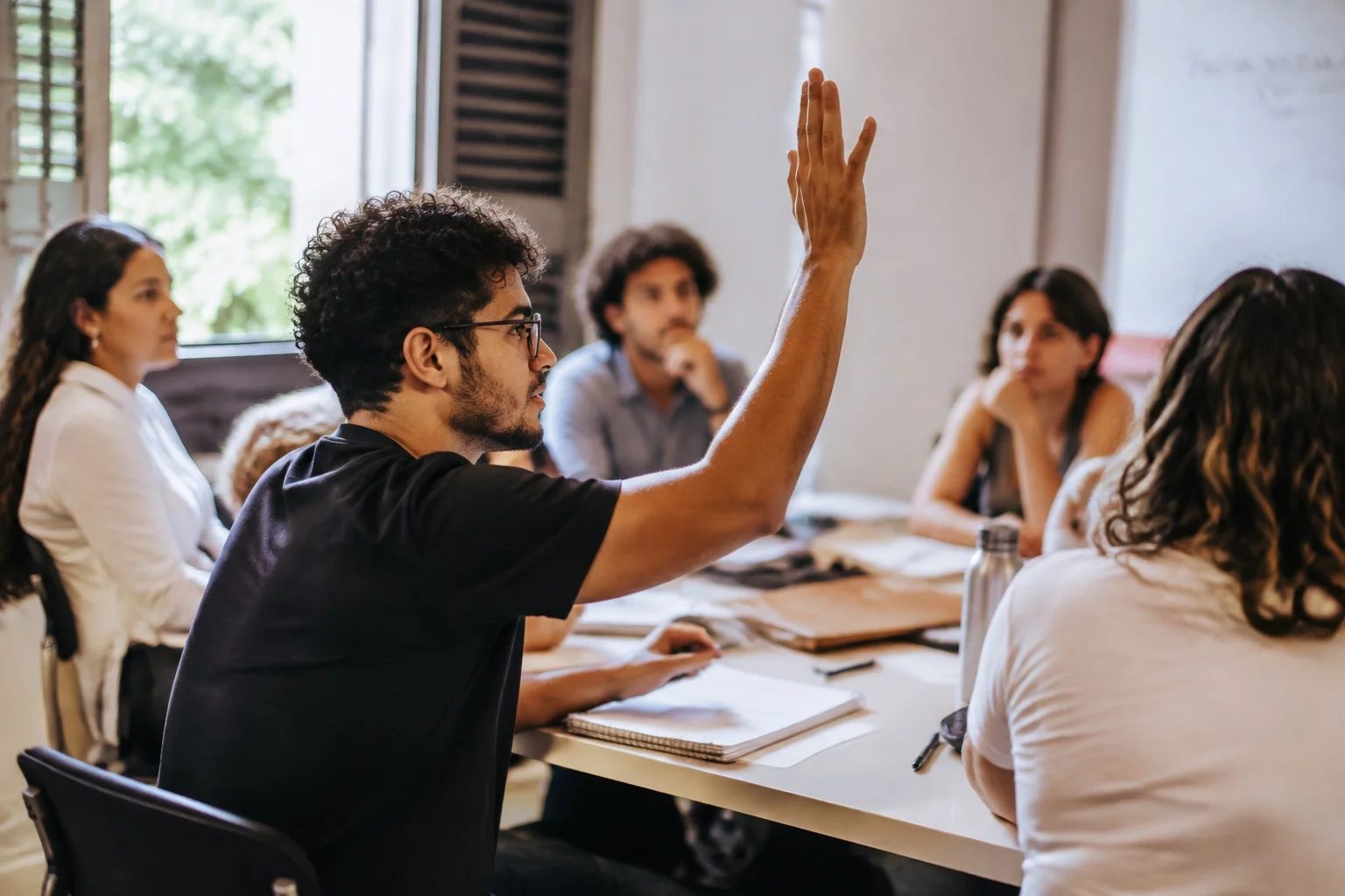 Estudante levantando a mão em uma mesa de seminário coberta de anotações